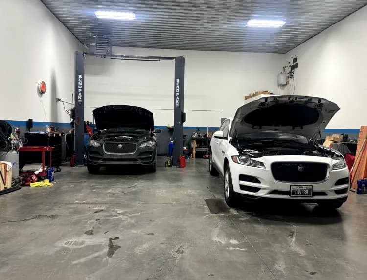 Two Jaguar F-Pace SUVs with hoods open in the service bays